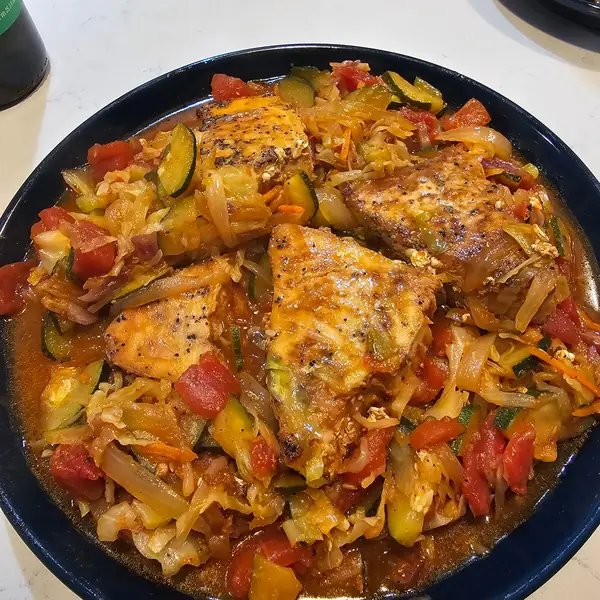 Seared entrée over stewed tomatoes, zucchini and cabbage